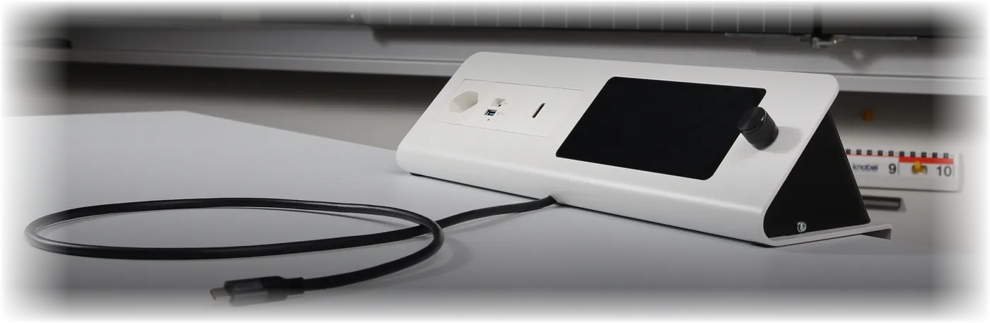 Die VEYCA Konsole auf einem Lehrerpult: weisses Pultgehäuse mit Steckdose, USB- und HDMI-Anschlüssen, Touchscreen und Drehregler, davor das aufgerollte USB-C-Anschlusskabel.